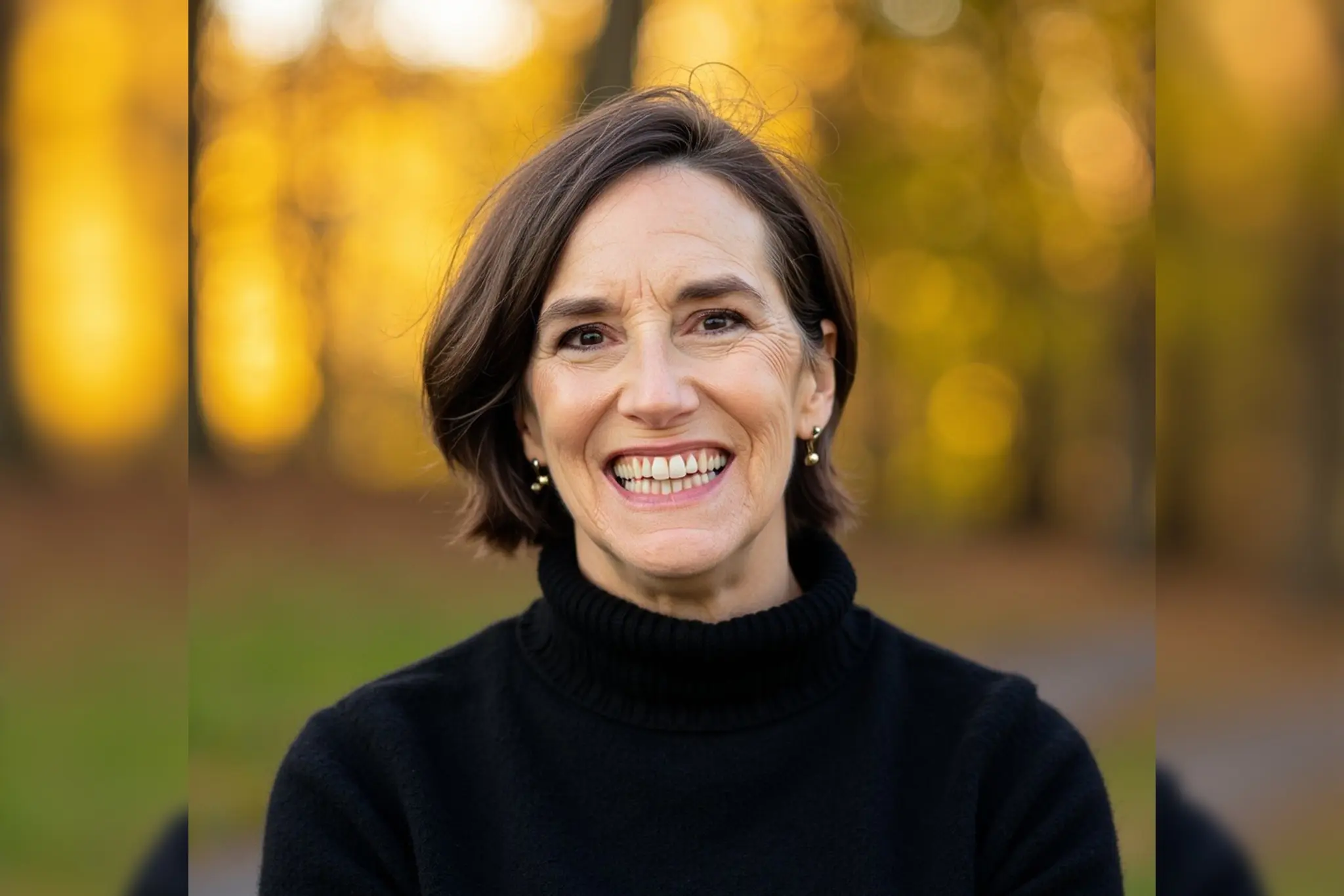 Smiling woman in black sweater outdoors with autumn background.
