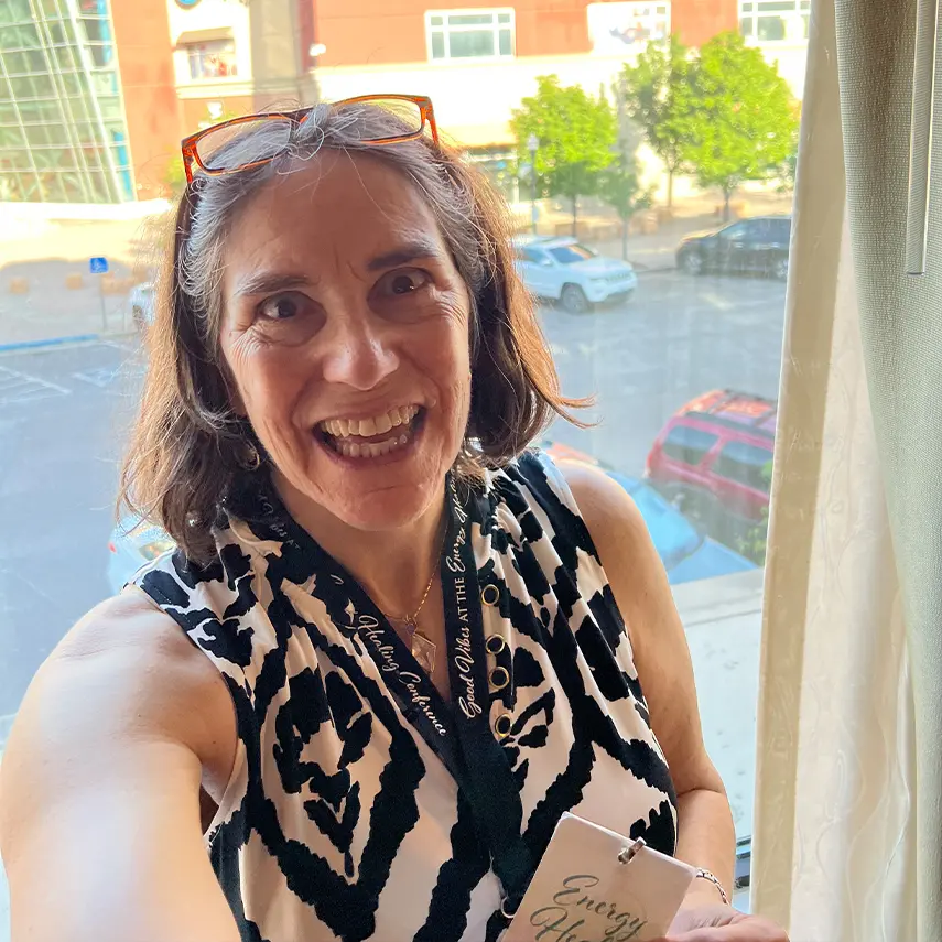 Smiling woman in a patterned sleeveless top near a window.